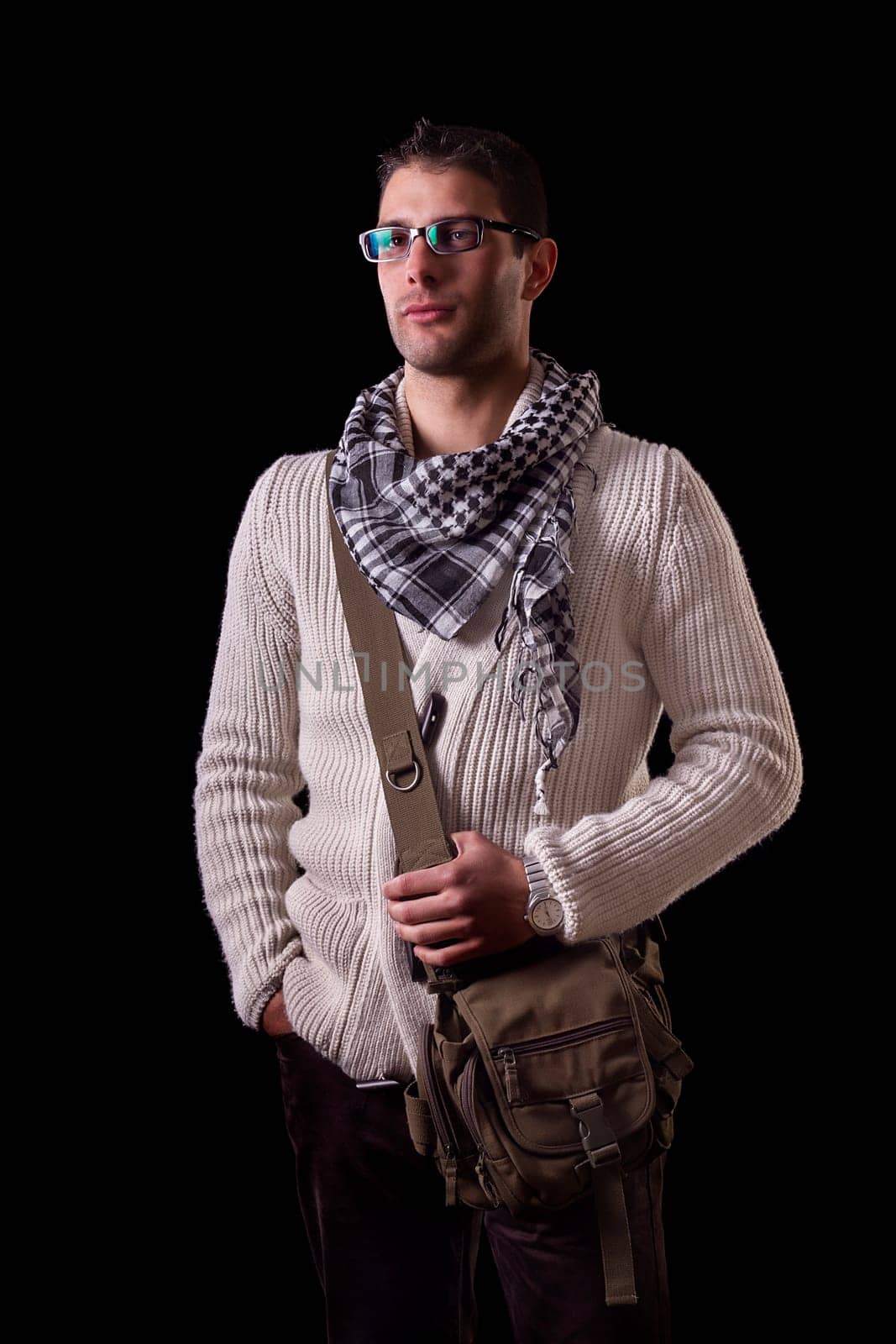 View of a young urban styled fashioned man standing isolated on a black background.