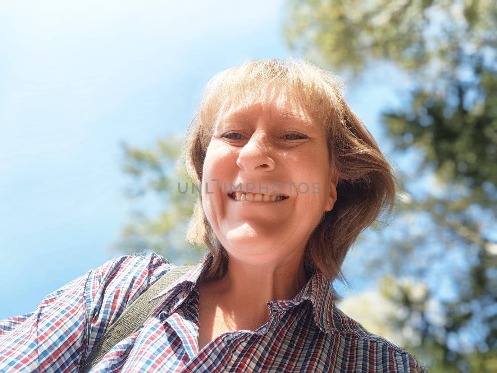 Blonde woman captures a cheerful selfie while exploring nature during an autumn adventure filled with colorful landscapes.