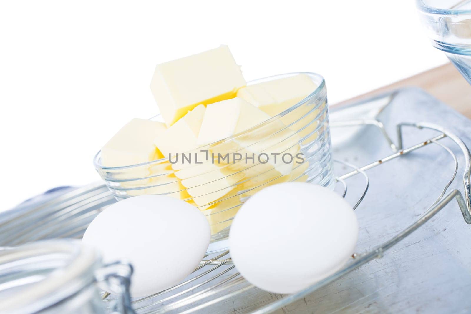 Butter in a glass bowl in front of white eggs on a cooling grid