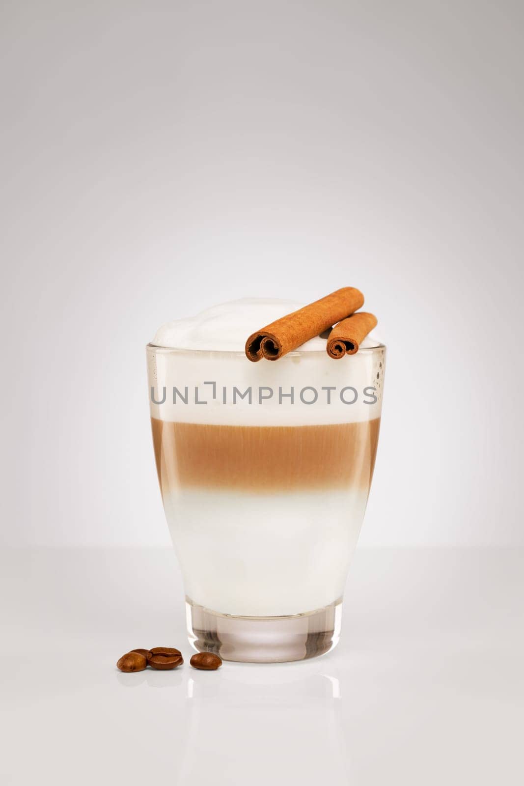 Latte macchiato with cinnamon sticks and coffee beans on a grey background