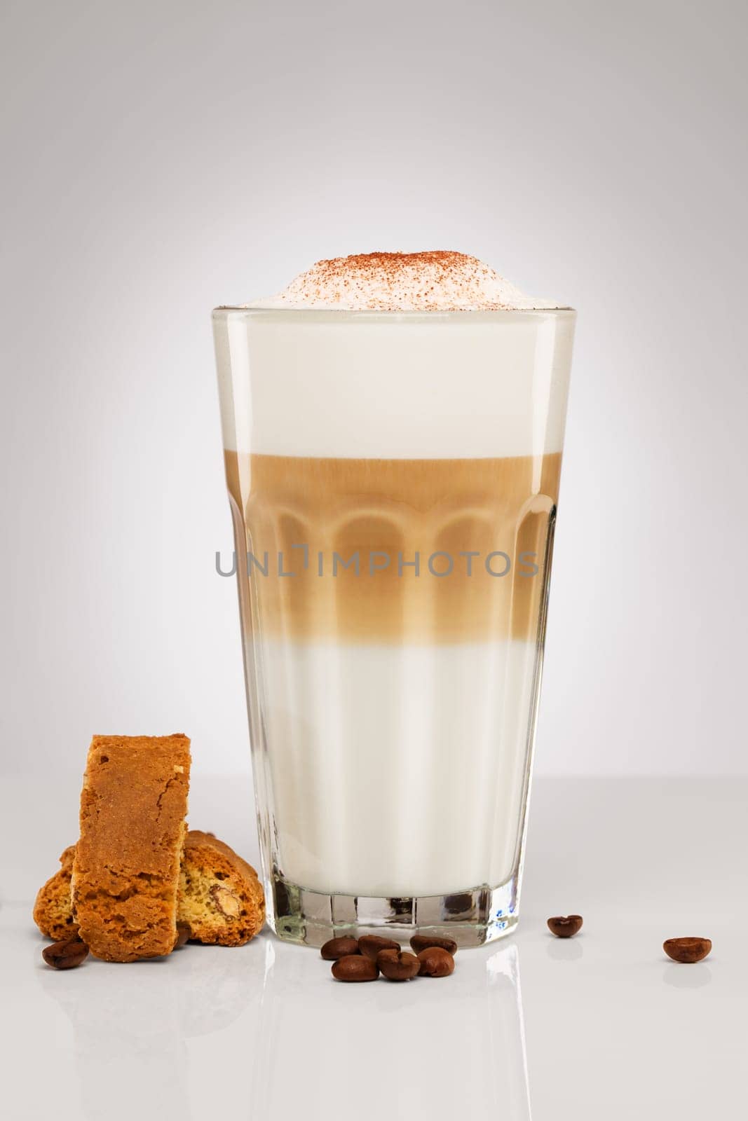 Latte macchiato with chocolate powder coffee beans and cantuccini biscuit on grey background