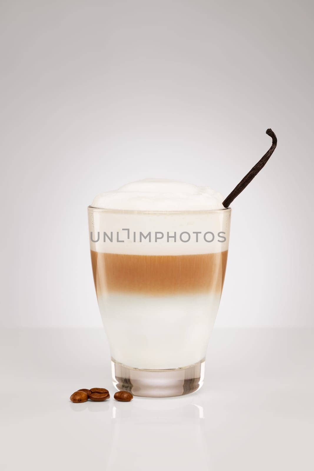 Latte macchiato with vanilla and coffee beans on grey background