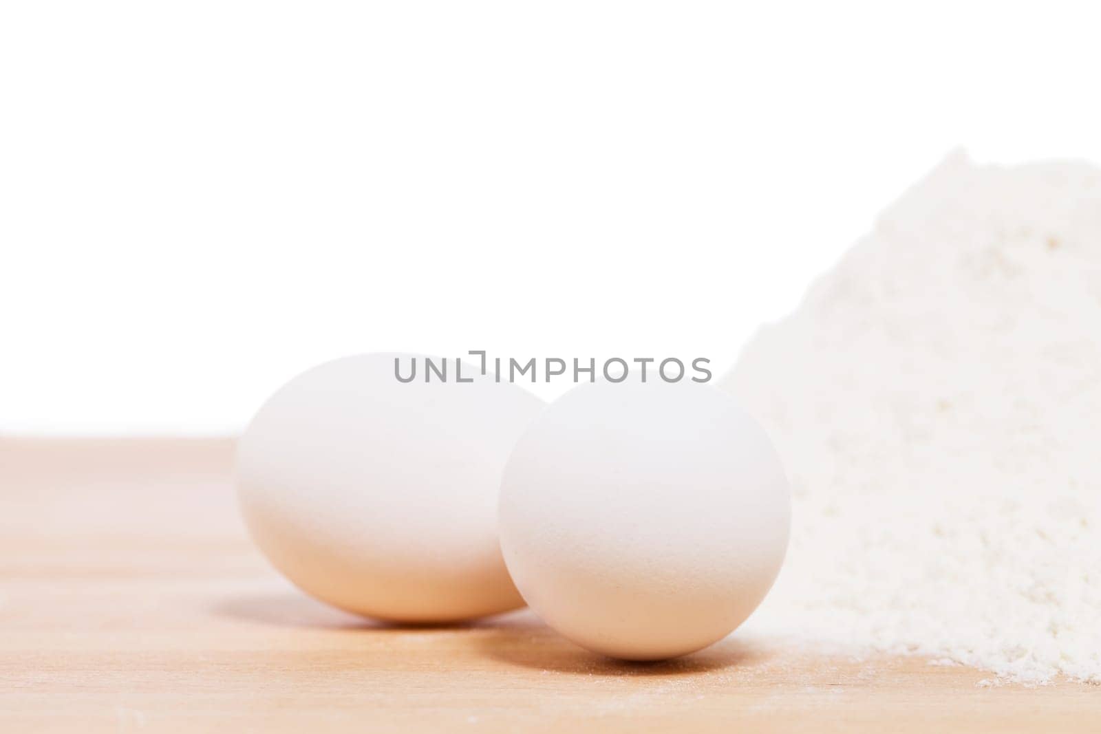 Close-up of white eggs on wood next to flour against a white background