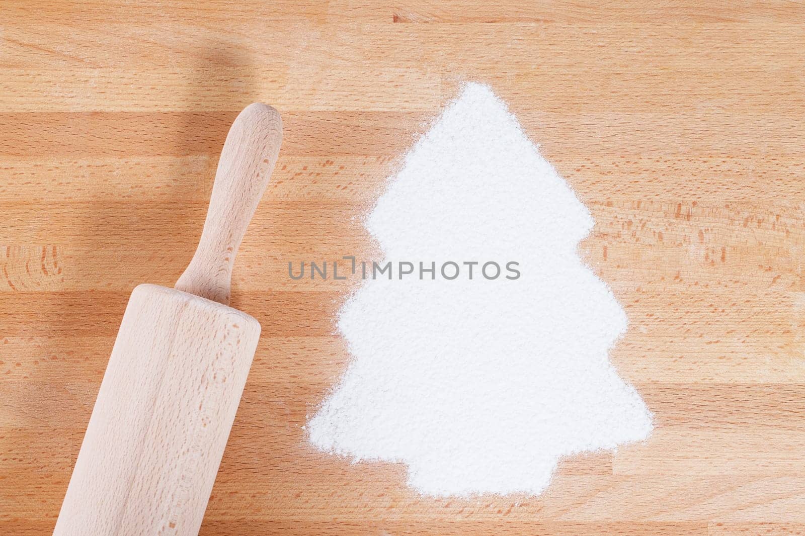 Flour in Christmas tree shape with rolling pin from above on wood