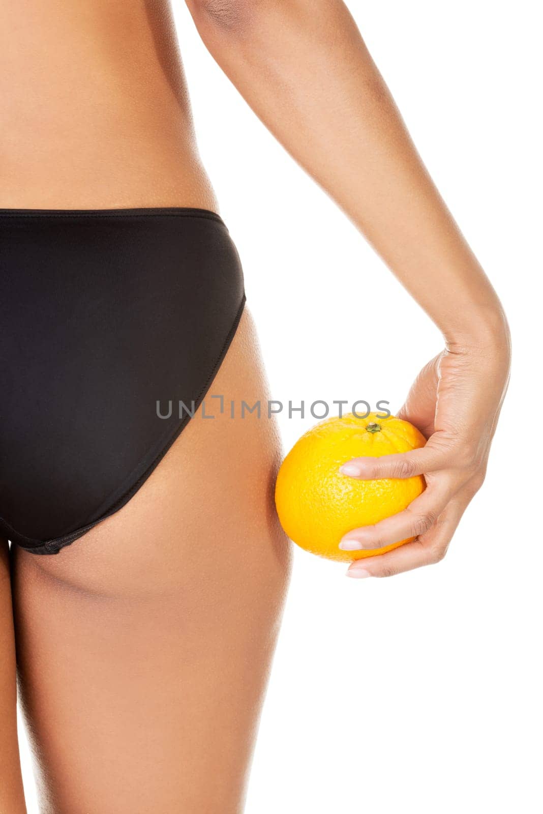 A girl holding an orange next to the buttocks, isolated on white
