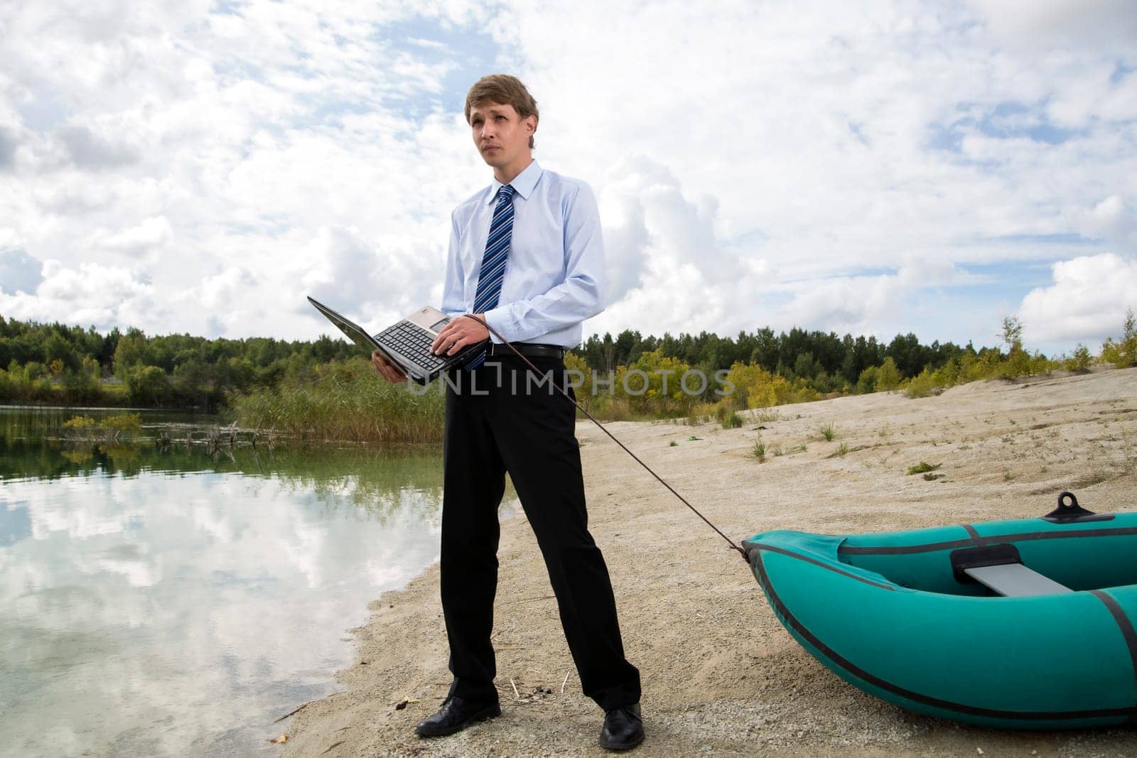 Dressed man drags boat over sandy lake shore