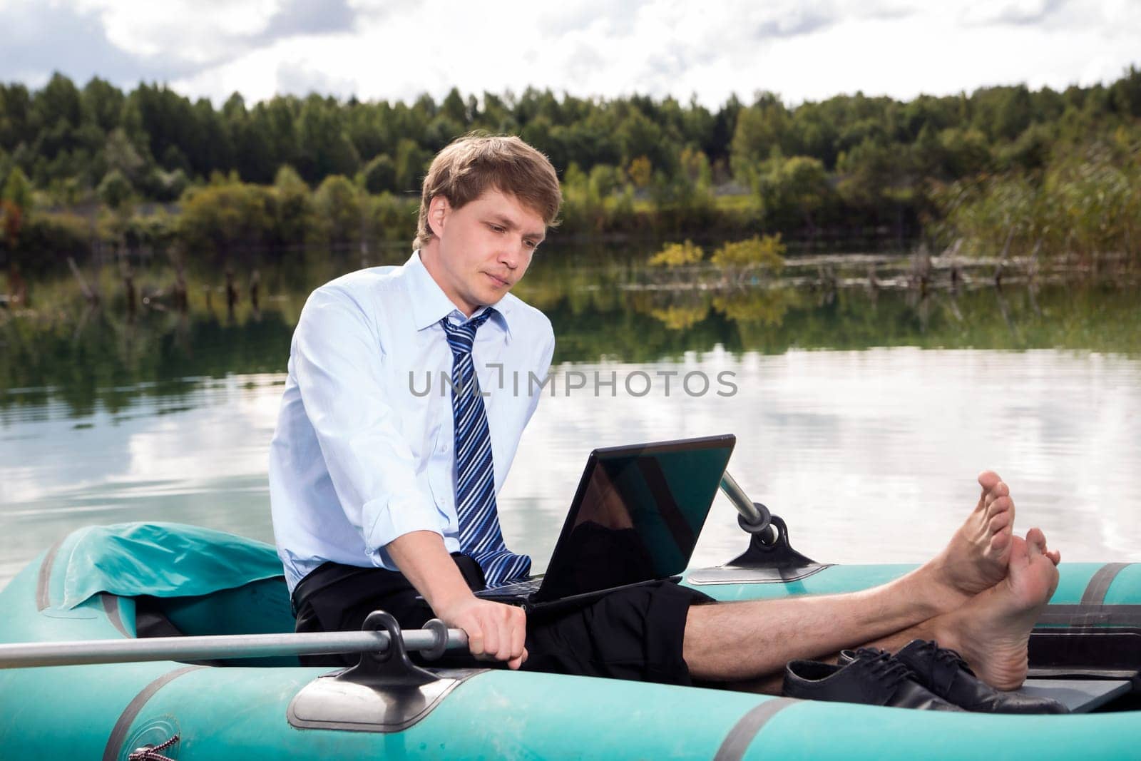 Dressed man in boat and reading from laptop
