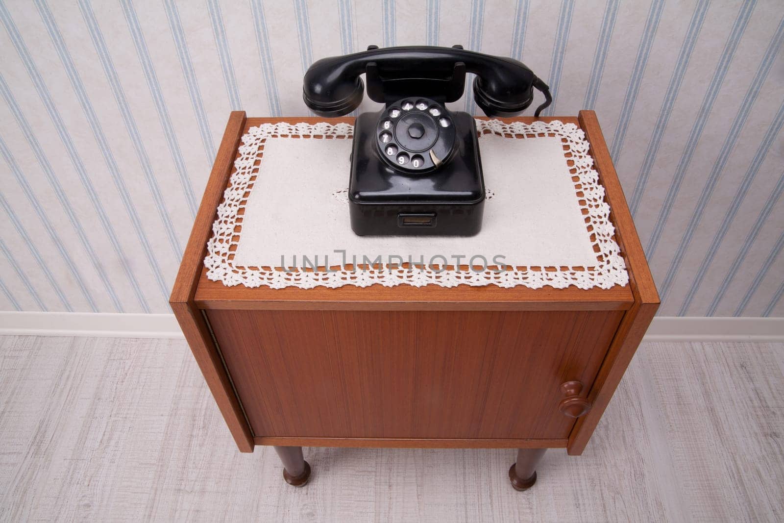 Black rotary dial telephone on a piece of furniture with old fashioned striped wallpaper