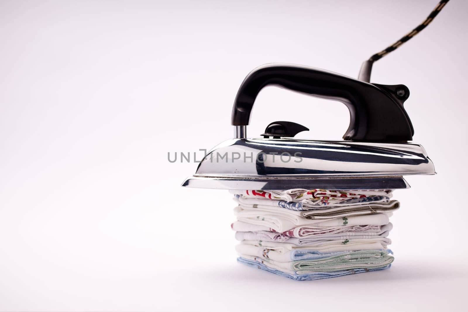 old fashioned electric iron with a black plastic handle and steel base lain on a pile of handkerchiefs in a natural light background