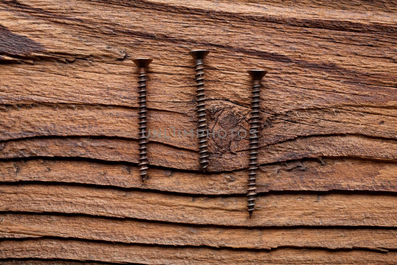 A set of three bronzed copper screws on a dark coarse-grained wooden background