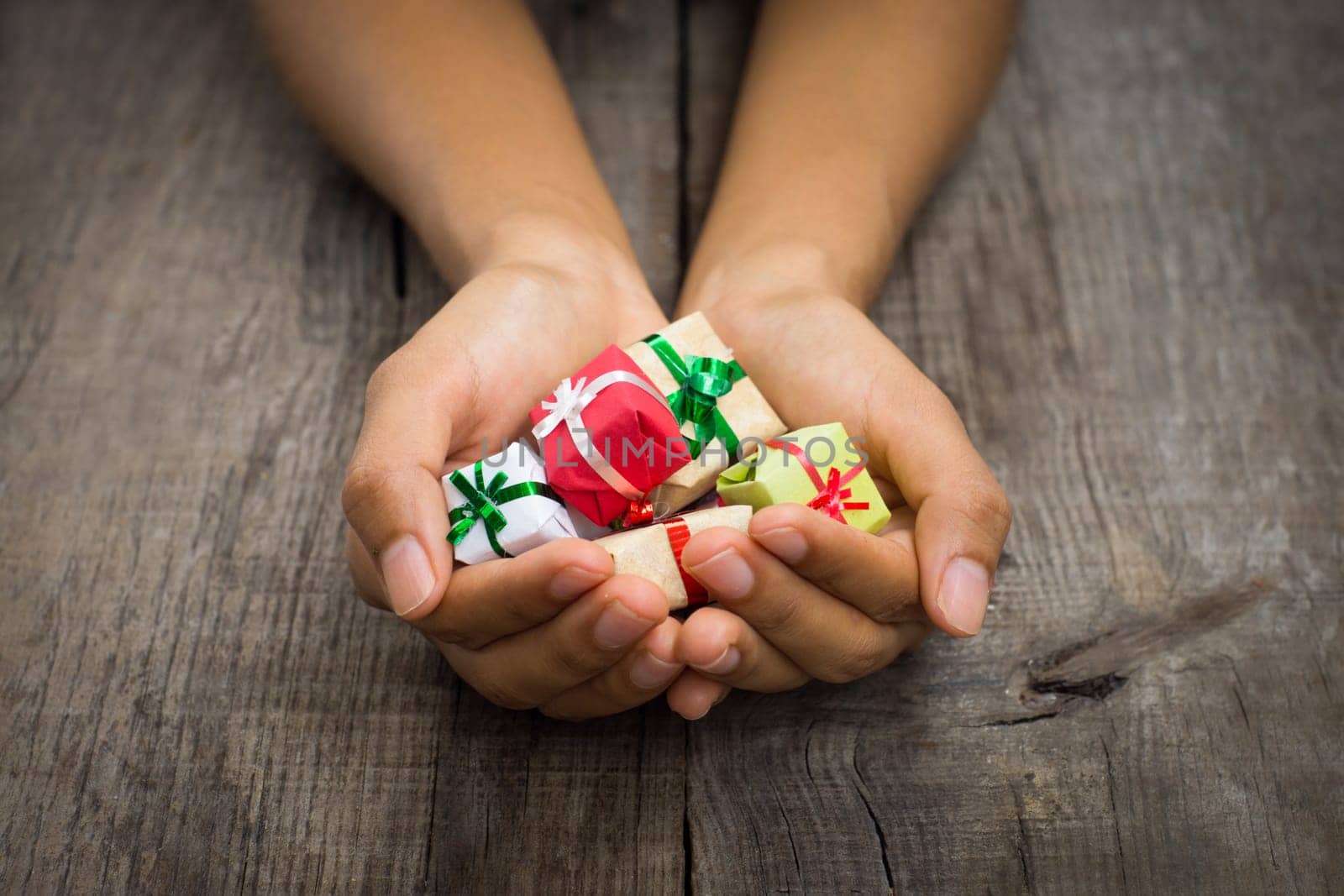 A person holding Miniature christmas presents on wood background.