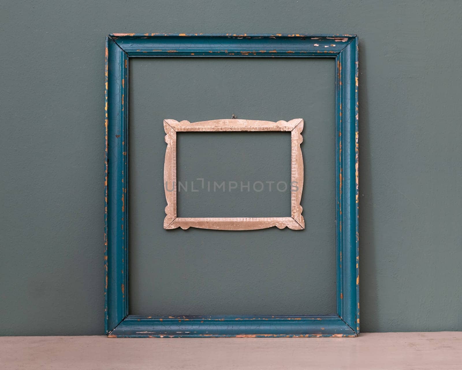 Two empty vintage picture frames, one painted blue, the other a smaller carved frame hanging on a teal colored wall for interior decor