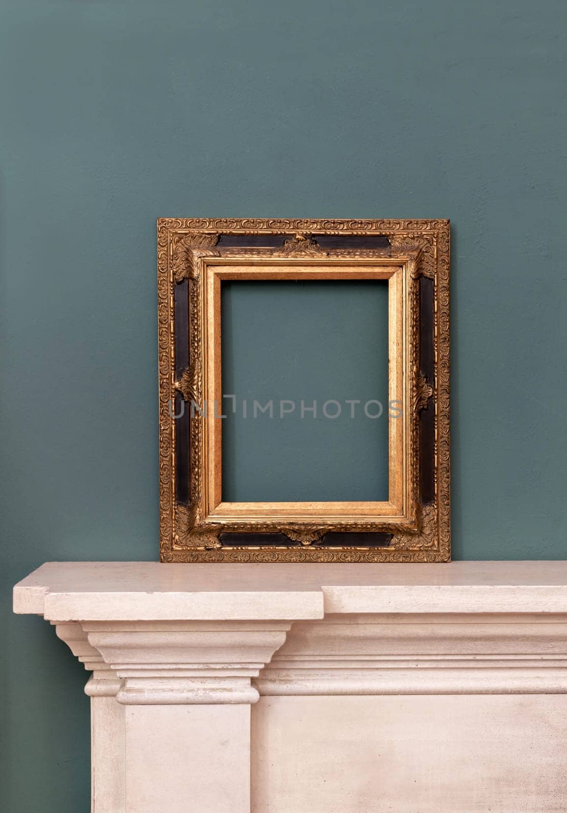 Gilded or golden empty rectangular vintage frame on a mantelpiece for a picture or painting leaning against a green wall