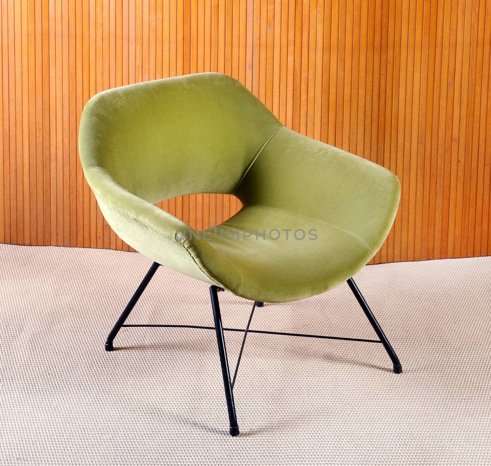 Upholstered green velvet curved vintage armchair with plush fabric and metal legs in a panelled living room