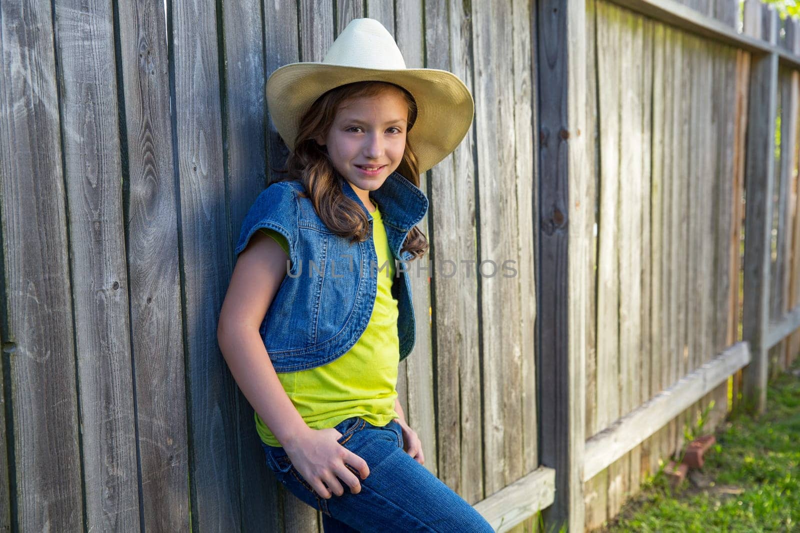 Children girl as kid cowboy girl cowgirl posing on wooden fence far west style