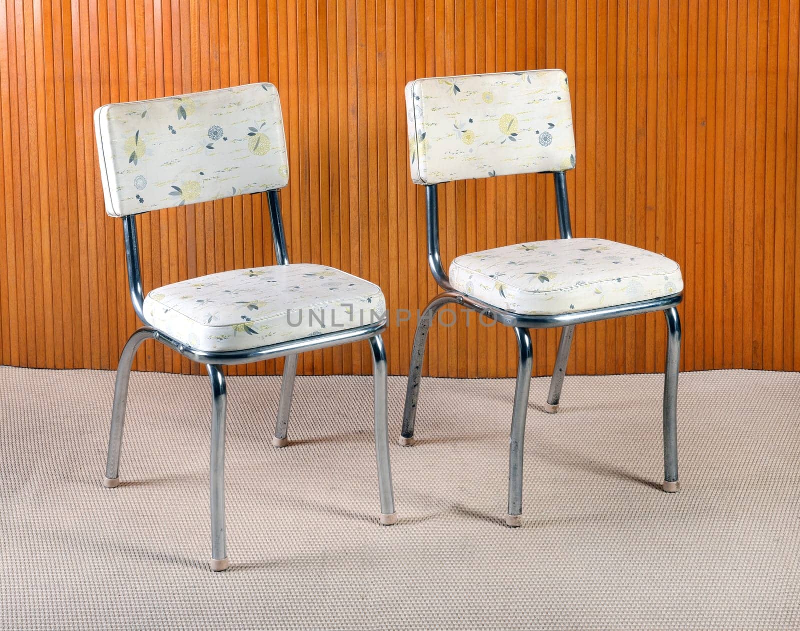 Still Life of Retro Chairs with Metal Bases and Patterned Seat Upholstery in Room with Beige Carpet and Wood Wall Paneling