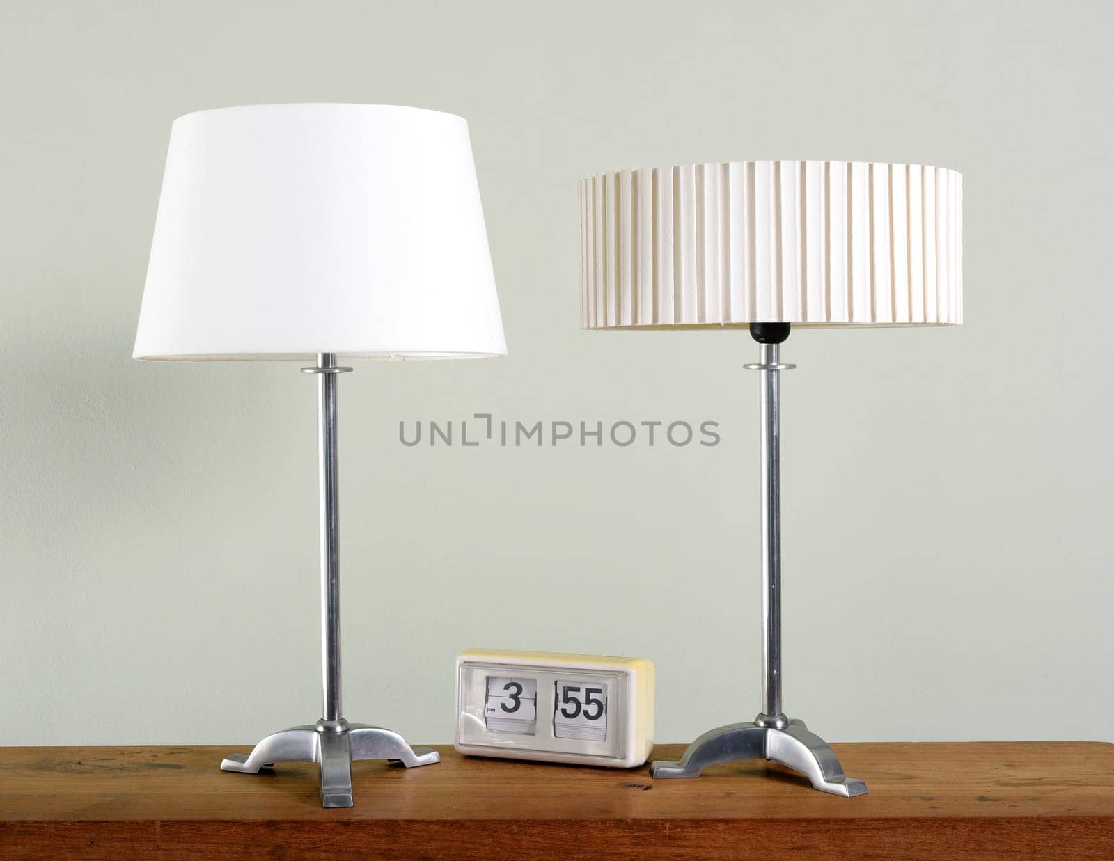 Two vintage metal lamps with different white shades alongside an old clock on a wooden table