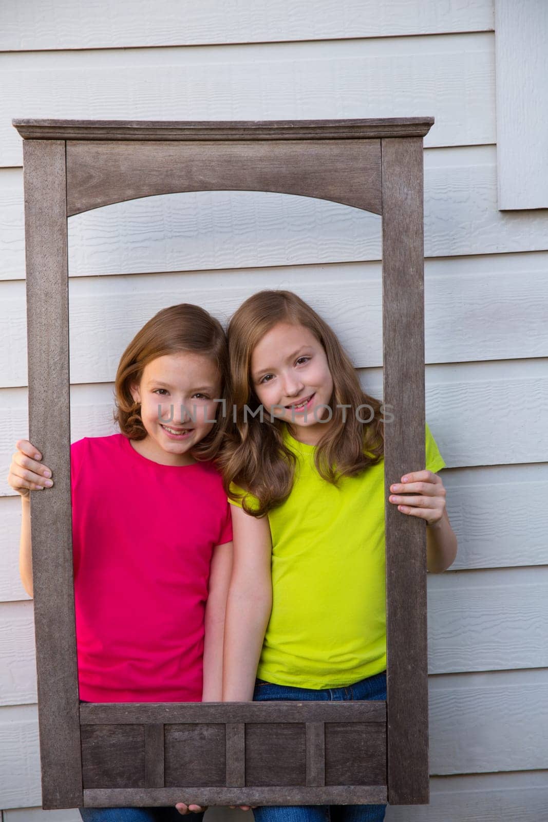 Twin sister girls posing with aged wooden border frame on white wall