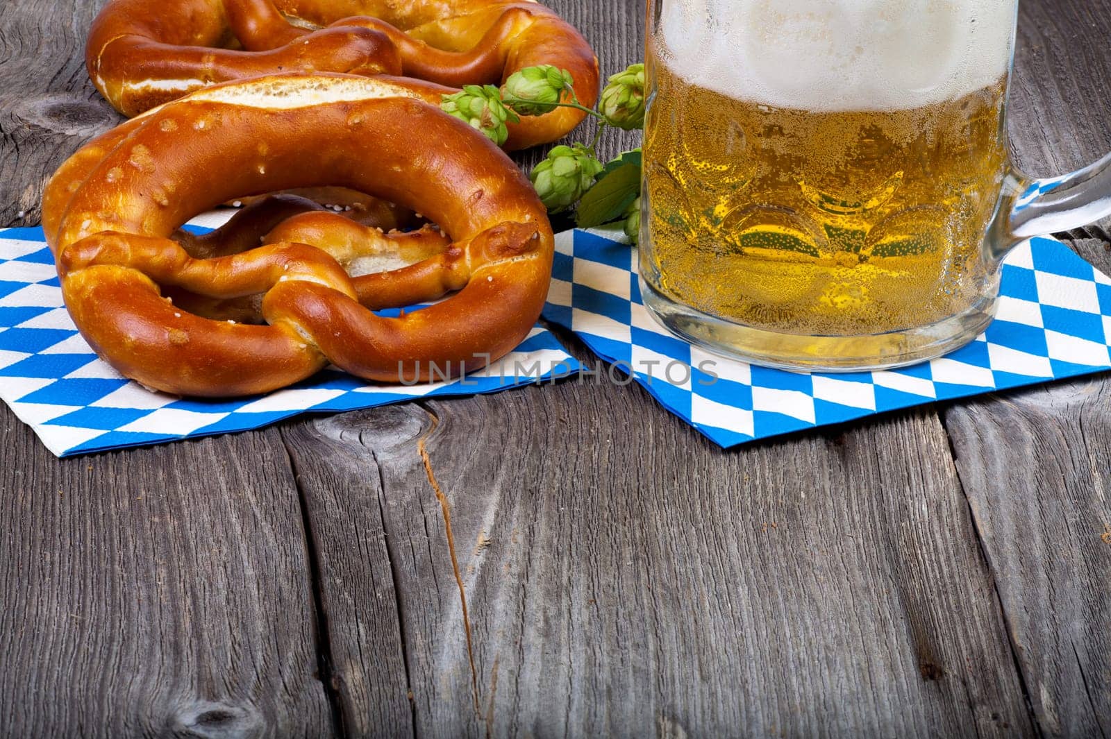 A glass of beer,pretzels and some hop cones on an old rustic wooden table