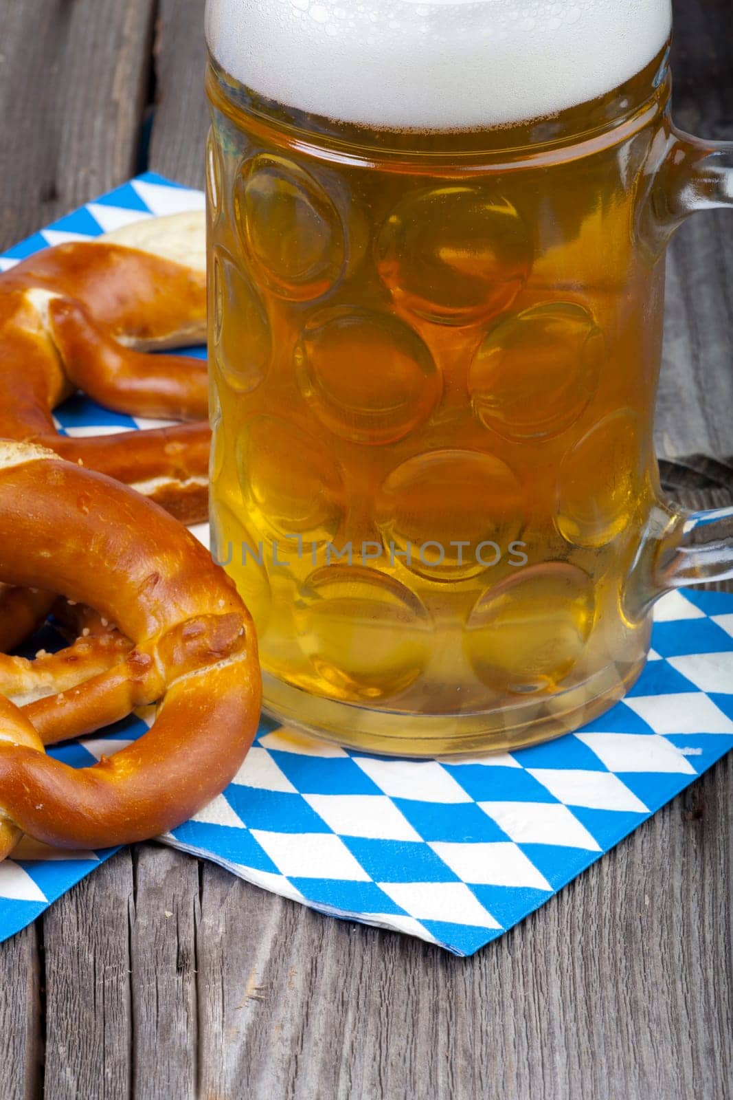 A large cold beer and pretzels on napkins with blue and white diamond pattern on an old rustic wooden table