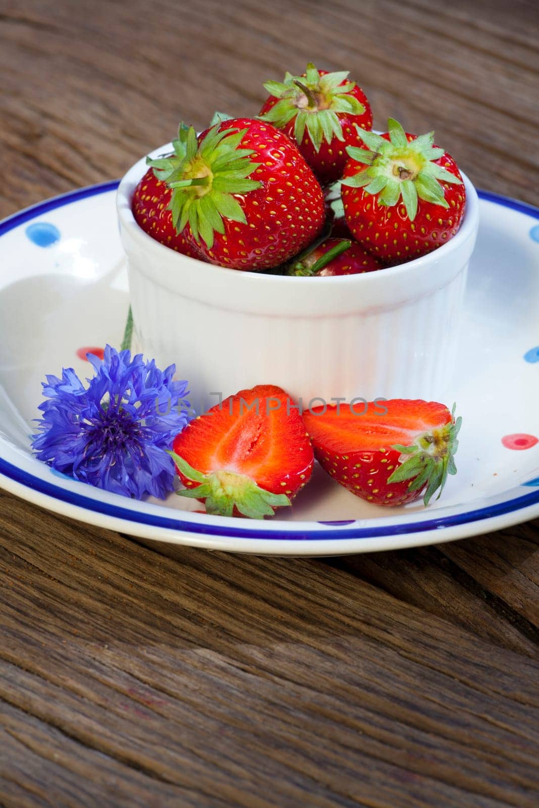 Small bowl of strawberries stands on a plate with a cornflower flower,text space in the lower part of the picture