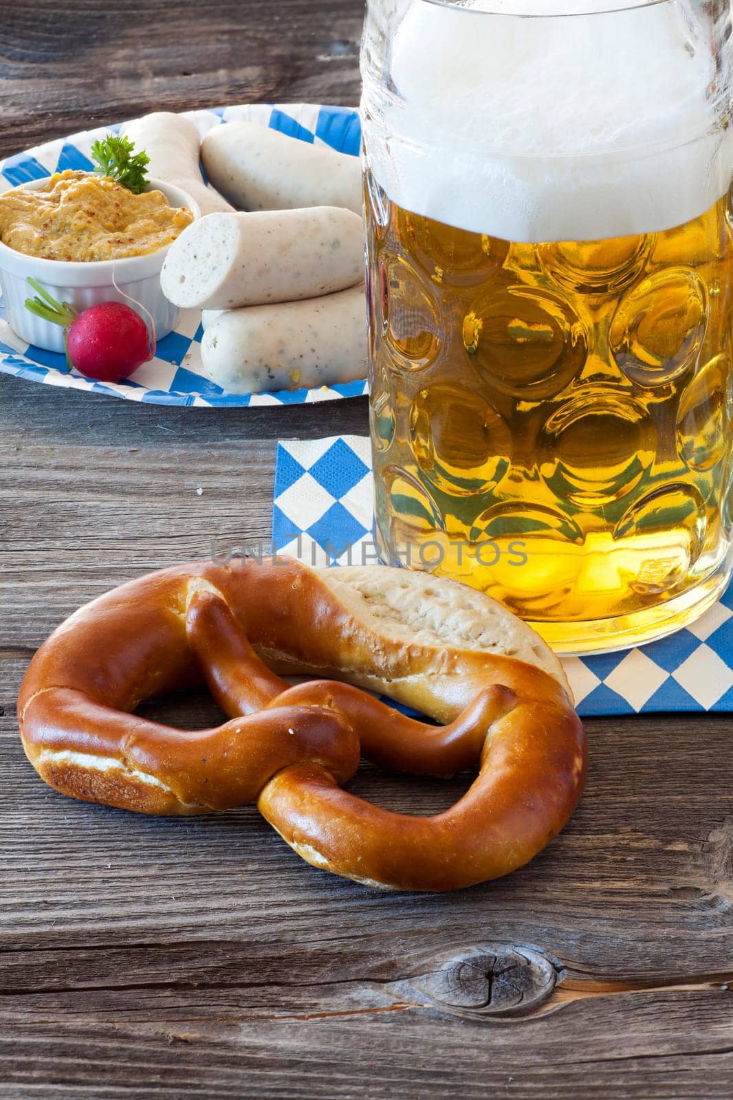 A cold beer in the Seidel,in front of it a pretzel and in the background a paper plate with white sausages and mustard
