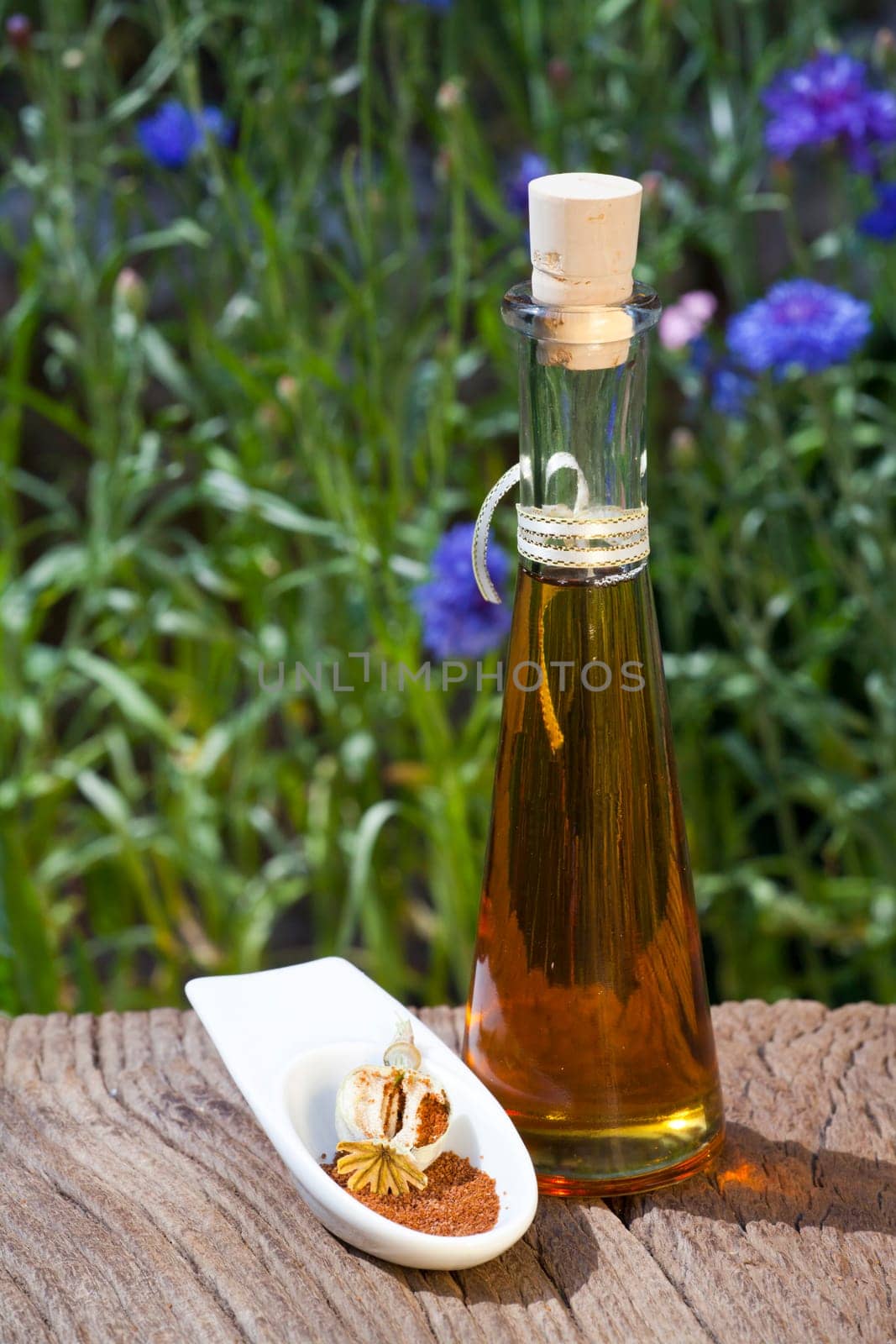 A small bowl of poppy seeds and a bottle of poppy seed oil stand on an old rustic wooden table