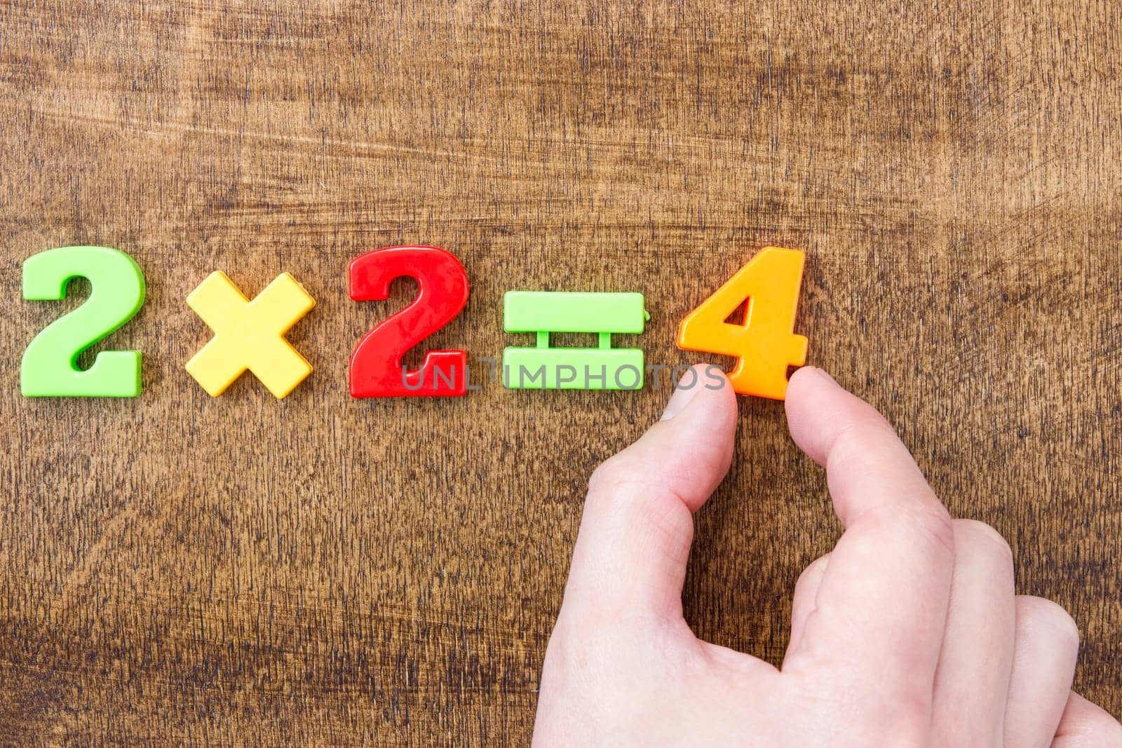 Solving simple mathematical formula. Hand with colored numbers on the wooden table