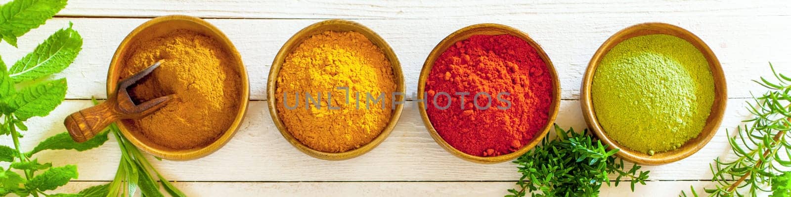 Banner with colourful spices and fresh herbs in wooden bowls on painted white boards, overhead view