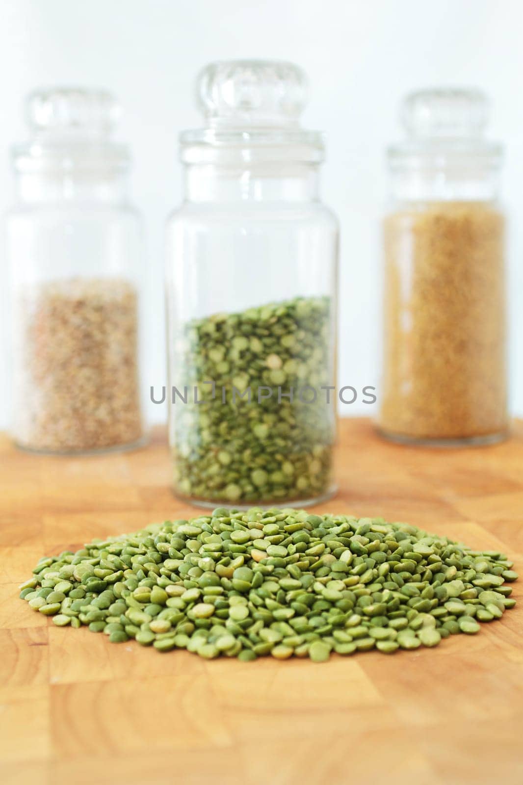Green split peas on a wooden board, with a jar of split peas and two jars of grains in the background