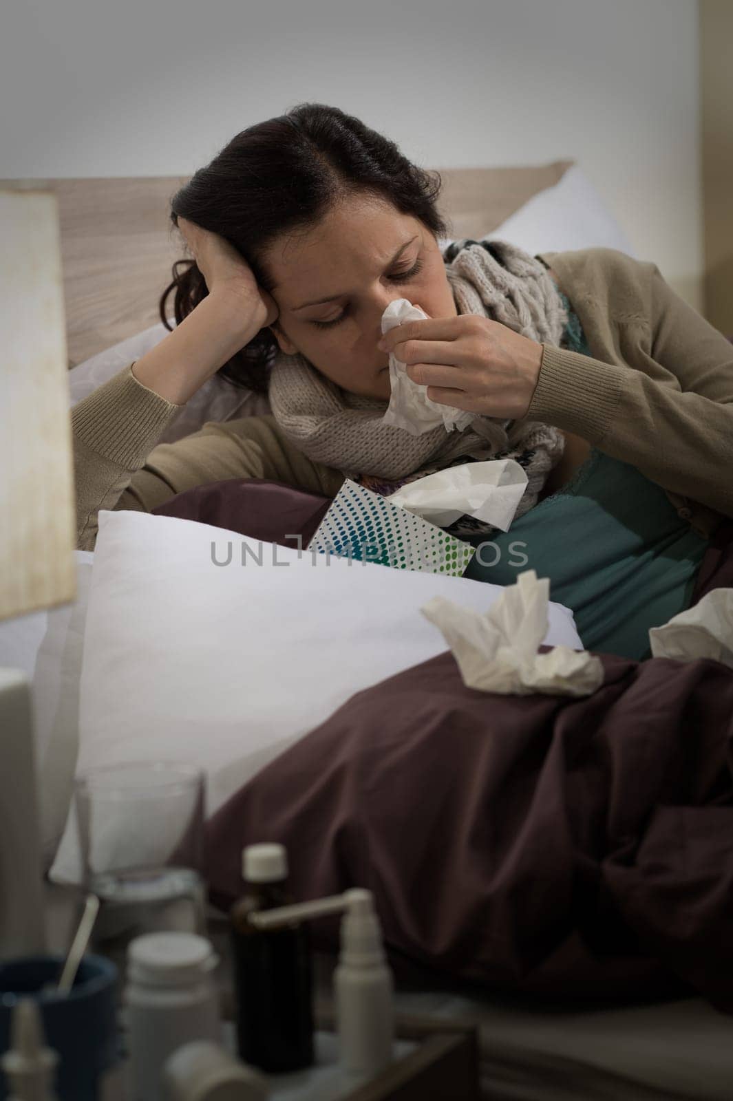Sick woman with flu sneezing blowing her nose in bed