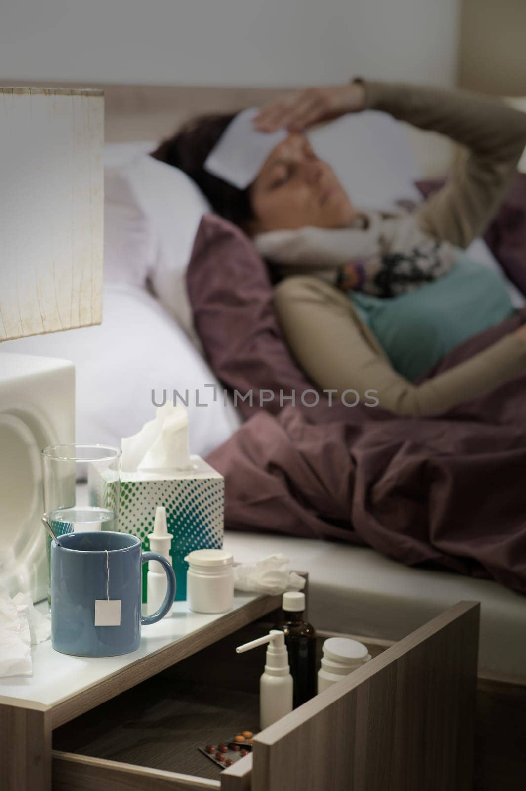 Flu medicines on bedside table beside ill woman in bed