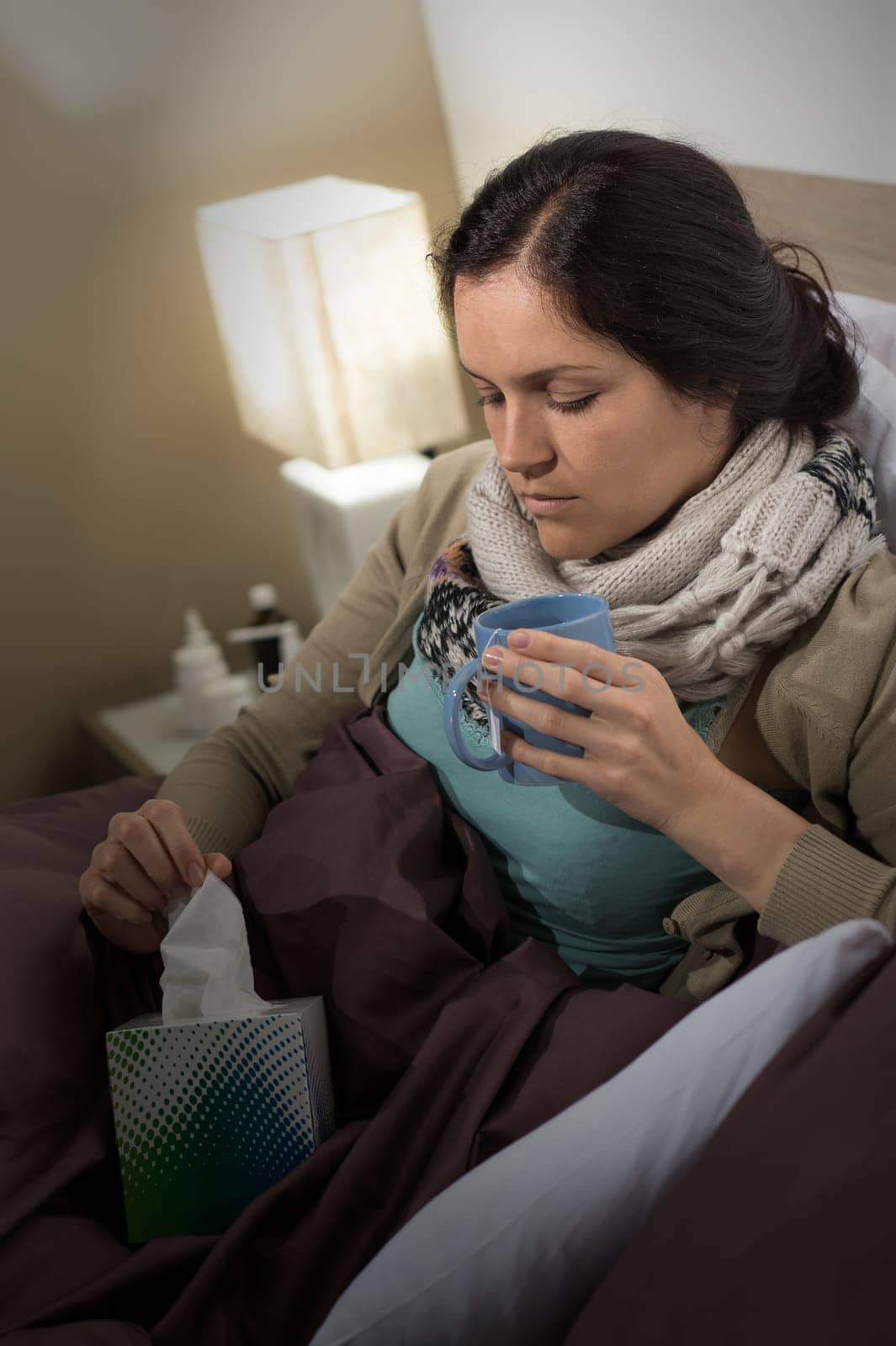Sick woman with cold flu in bed holding tissue and tea