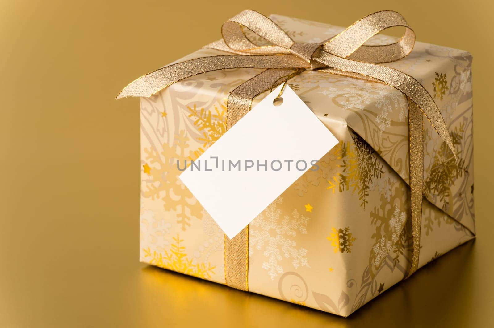 Christmas present with ribbon and blank tag on gold background copyspace