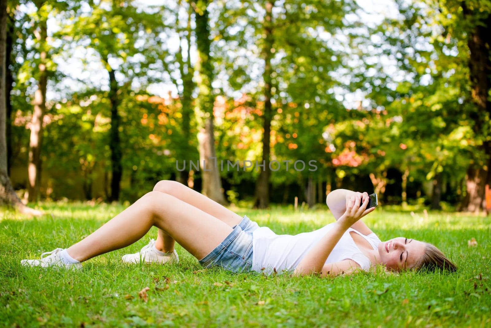 Mobility - teen girl lying on grass and working with smartphone