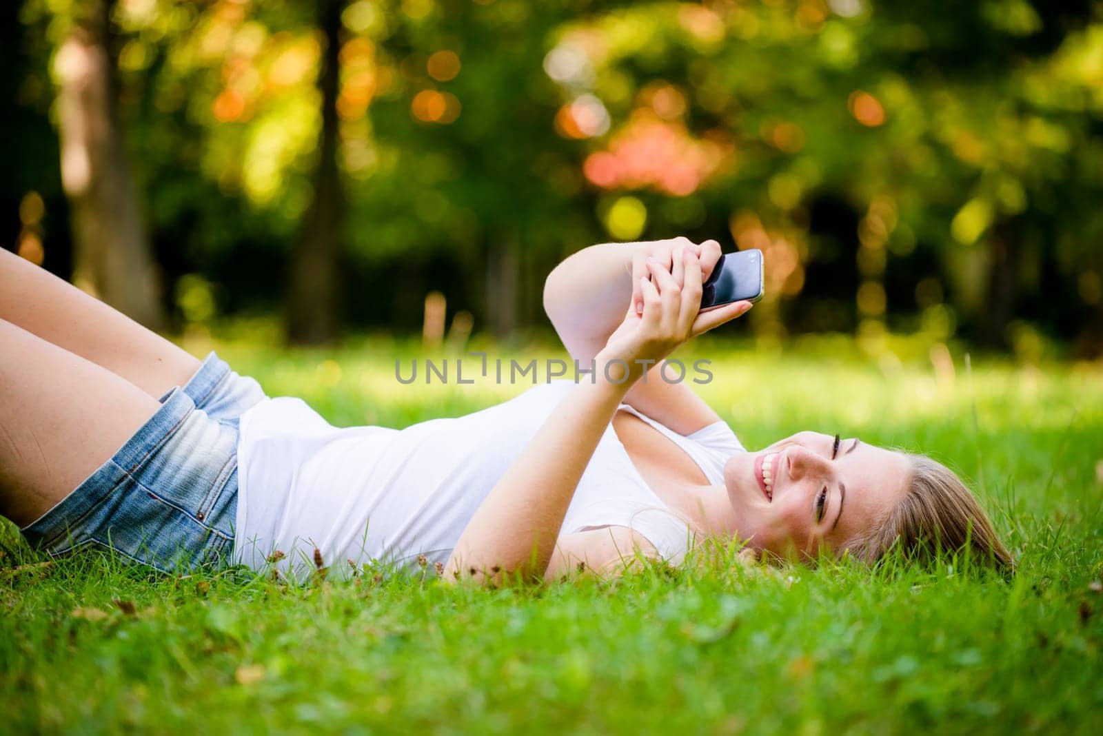 Teen lifestyle - young woman lying on grass and working with smartphone