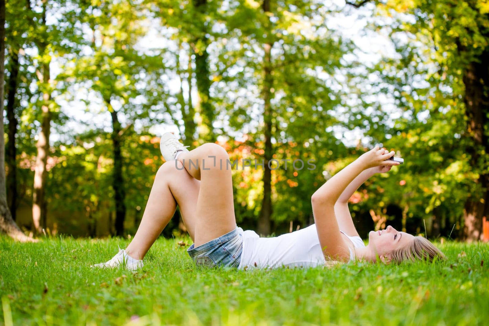 Mobility - teen girl lying on grass and working with smartphone