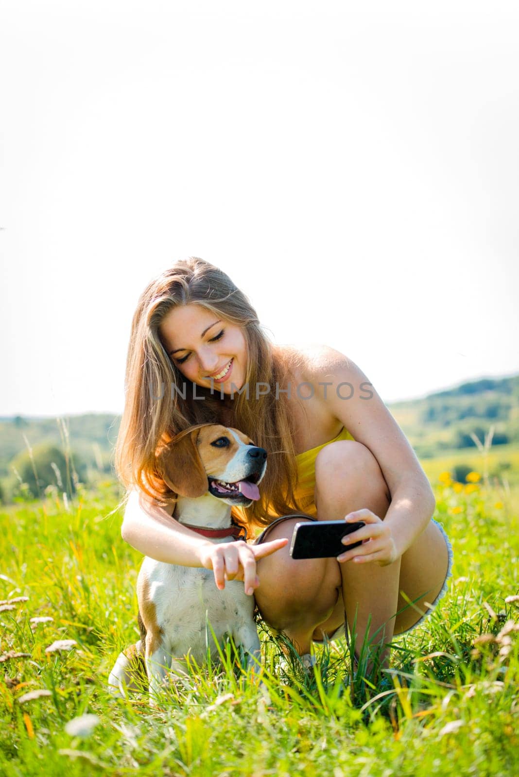Teen girl showing something to her dog on smart-phone, outdoor in nature