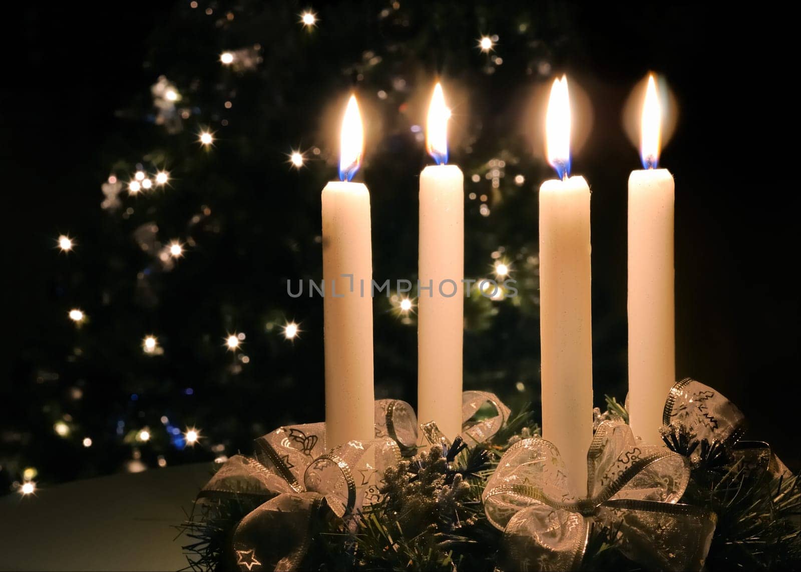 Christmas advent wreath with burning candles. Lights on x-mas tree in background