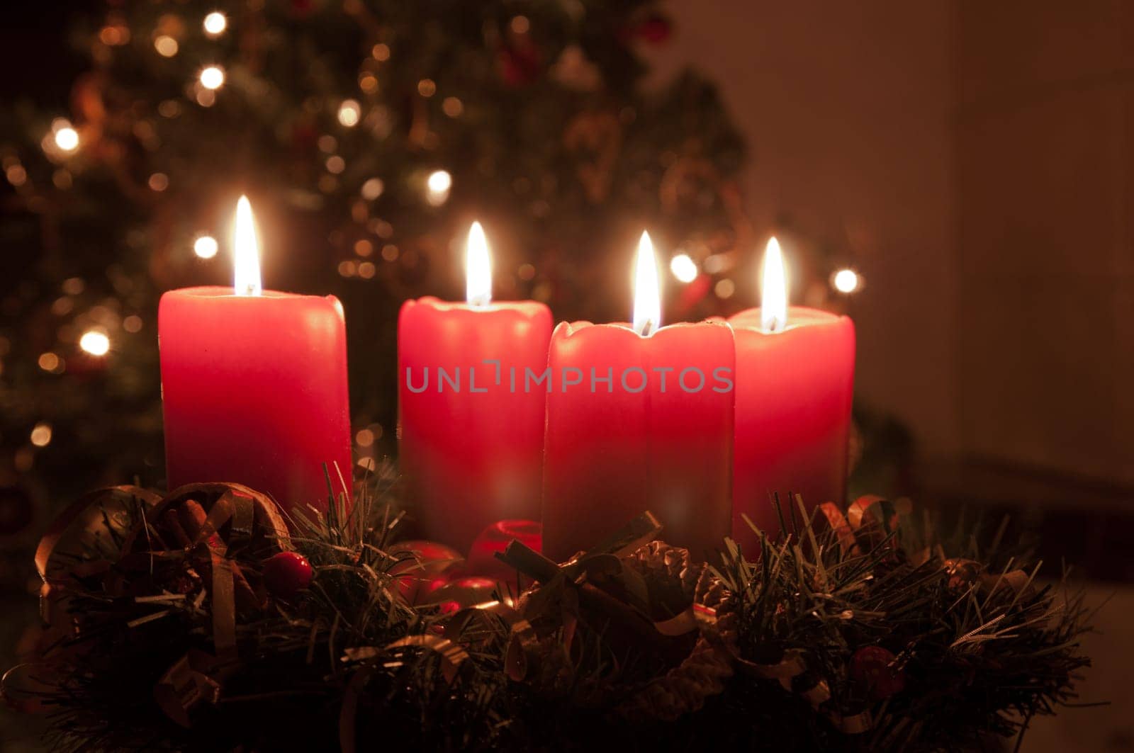 Christmas advent wreath with red burning candles. Lights on x-mas tree in background