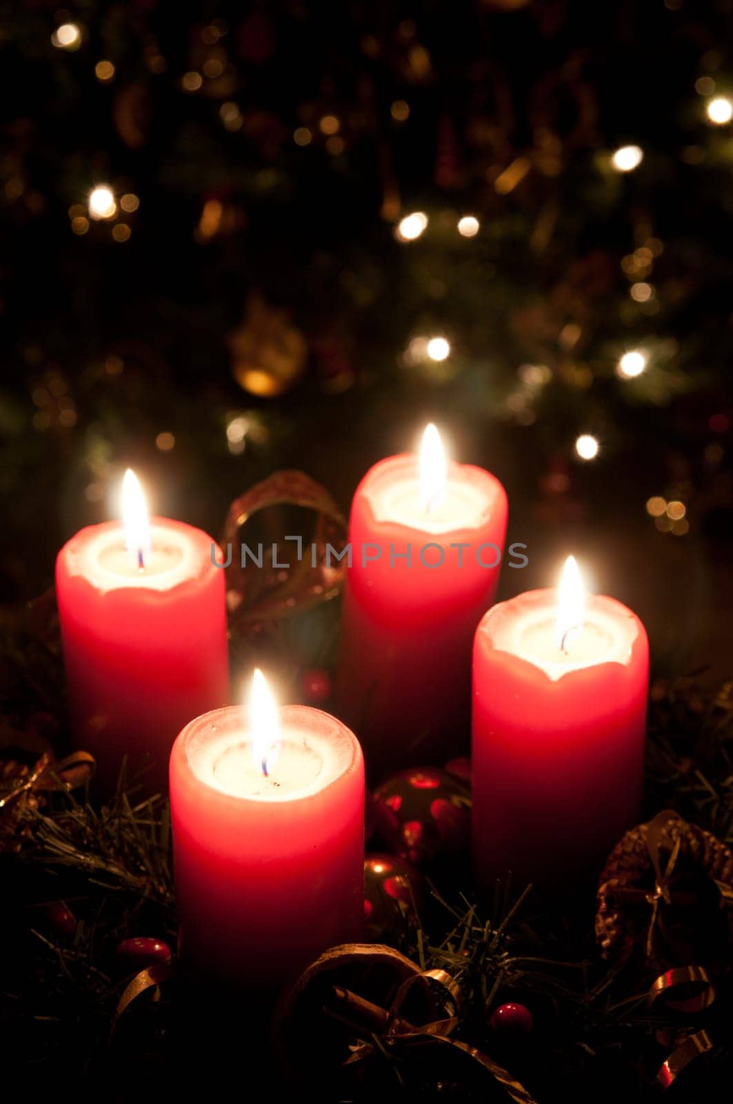 Christmas advent wreath with red burning candles. Lights on x-mas tree in background