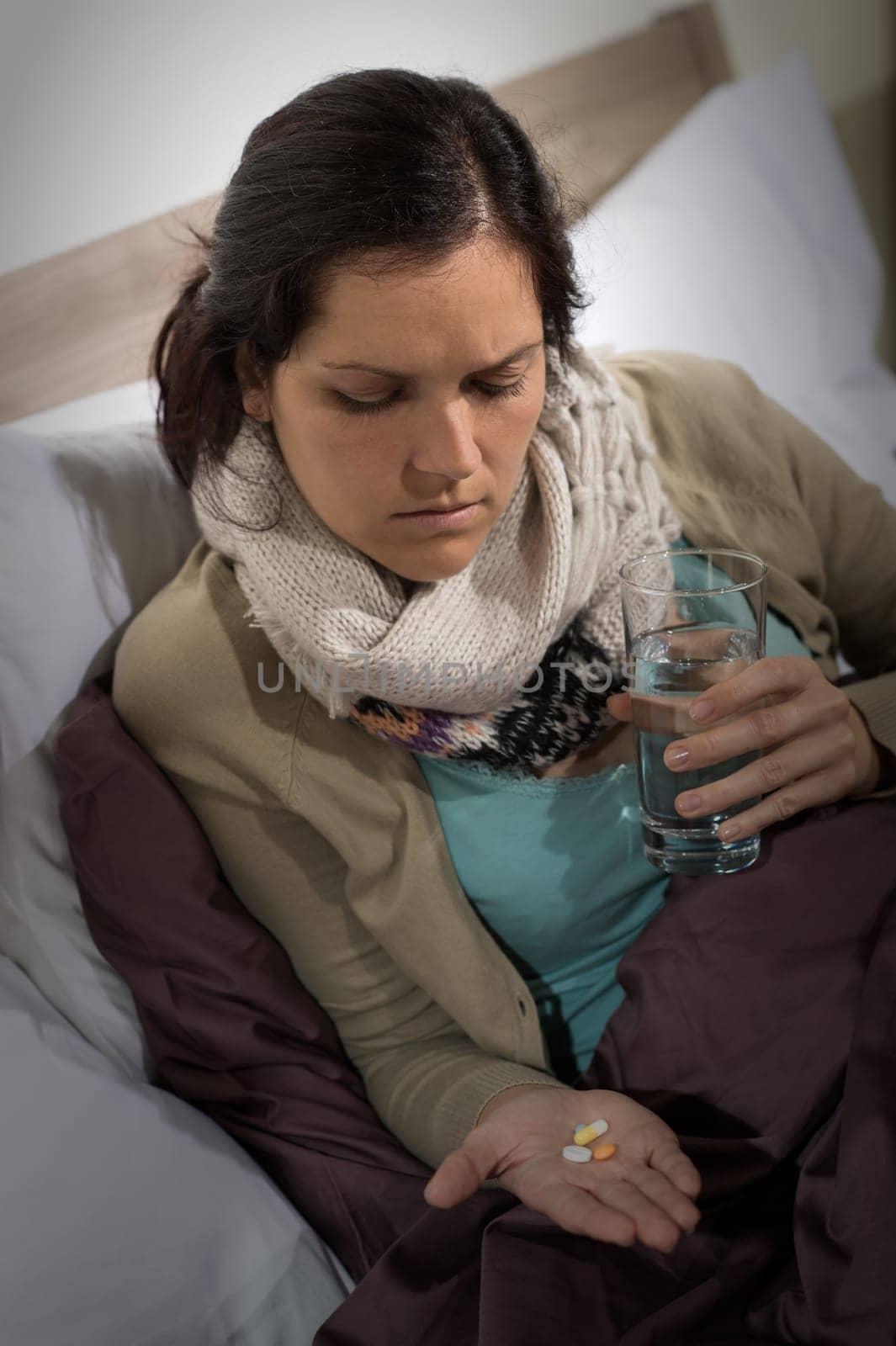 Sick woman holding and looking at medicine pills flu cold