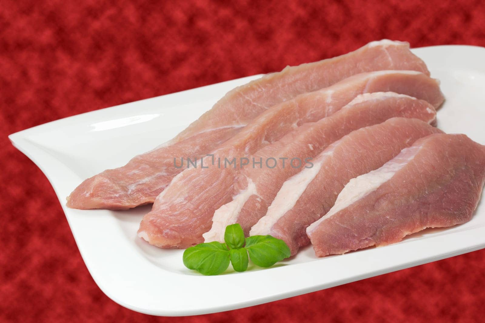Sliced ​​pork on a white plate. Red background.