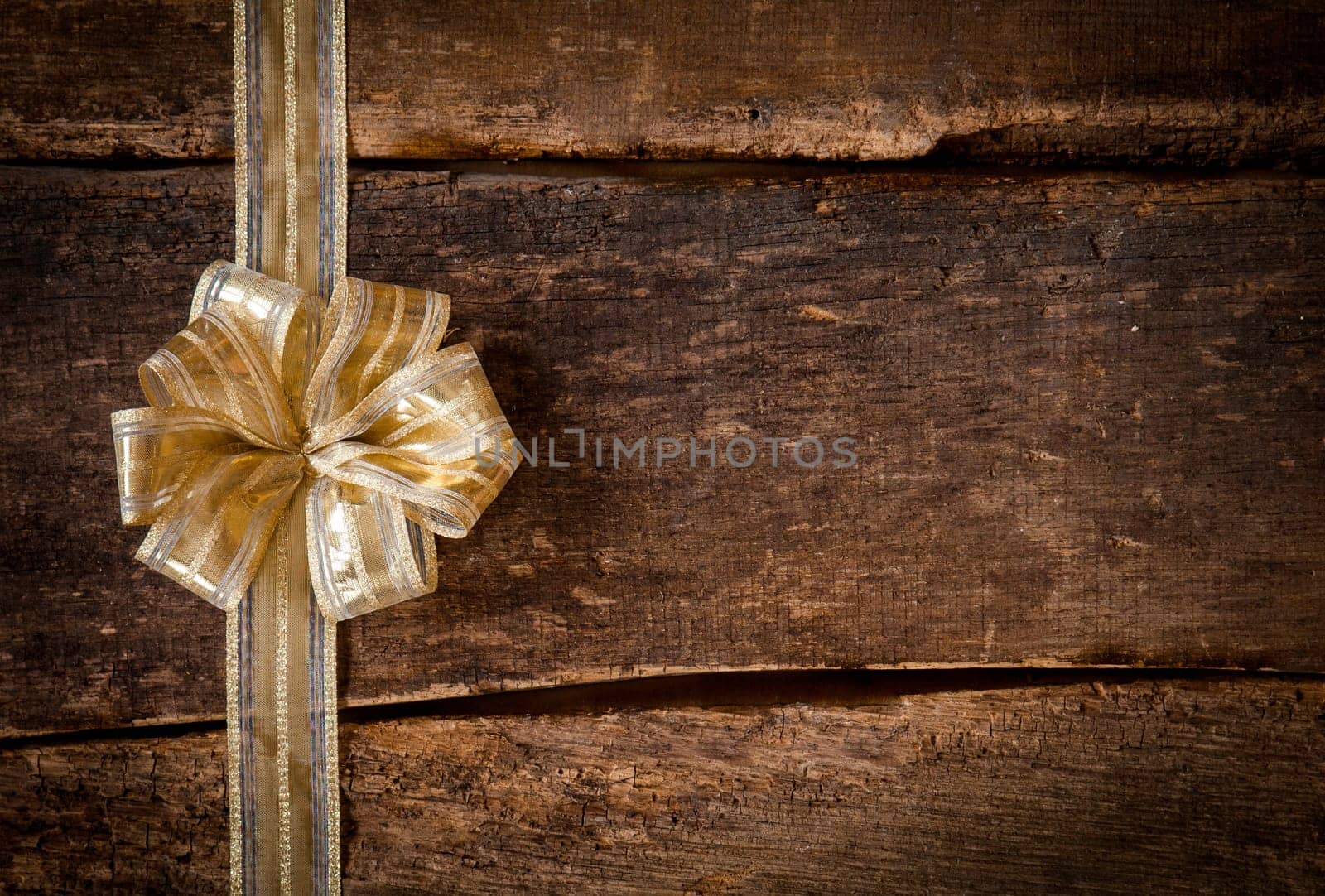 Festive gold ribbon and bow border to the left of the frame over a grunge dark textured rustic wood background with copyspace for your Christmas, anniversary or birthday wishes or invitation
