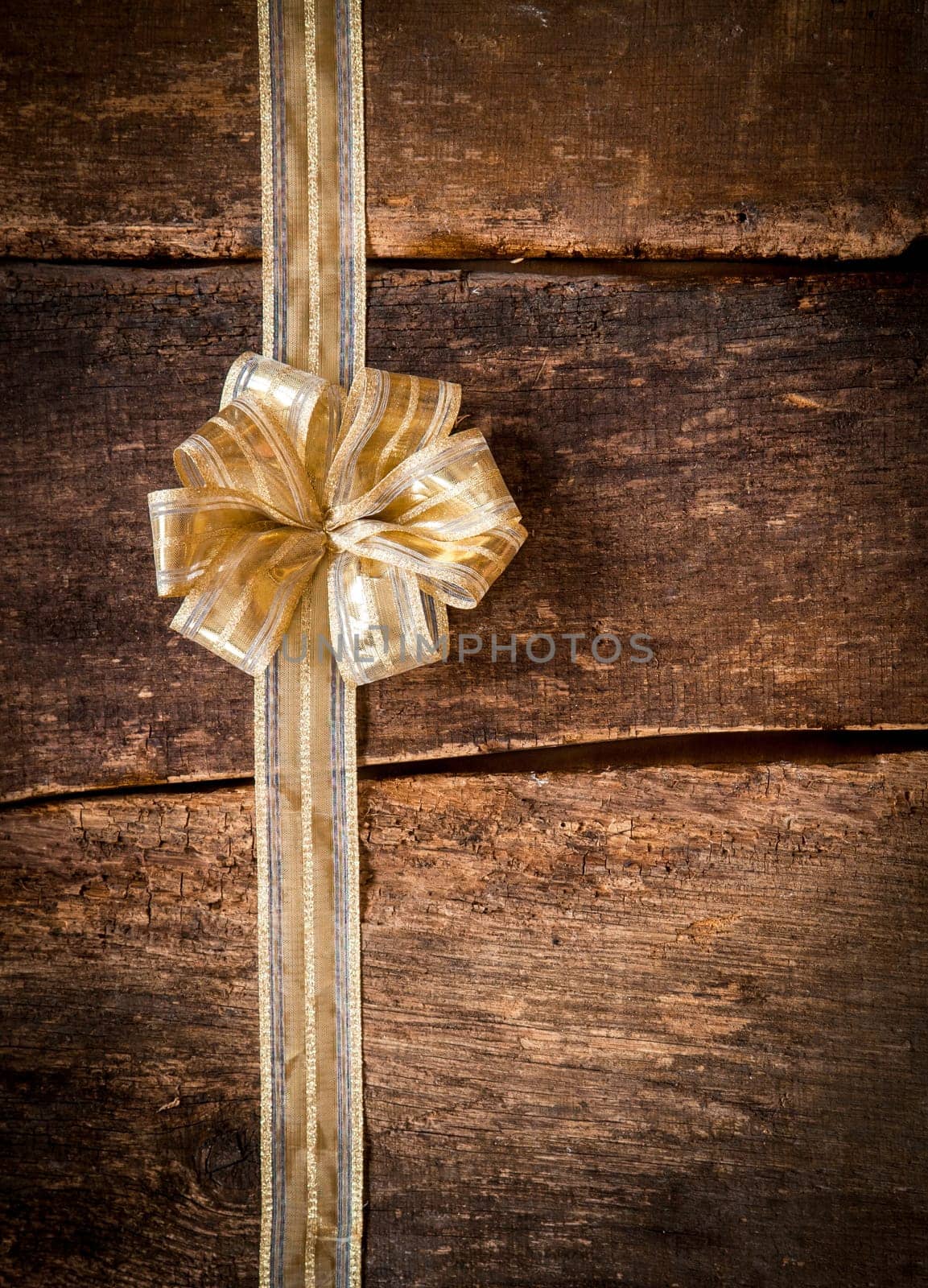 Pretty ornamental gold bow and ribbon over dark textured wooden planks with copyspace for your text or Christmas, anniversary or birthday greeting