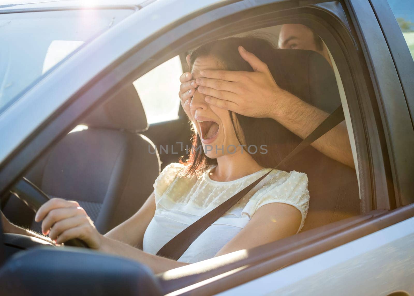 Young couple in car - man covering eyes of his girlfriend
