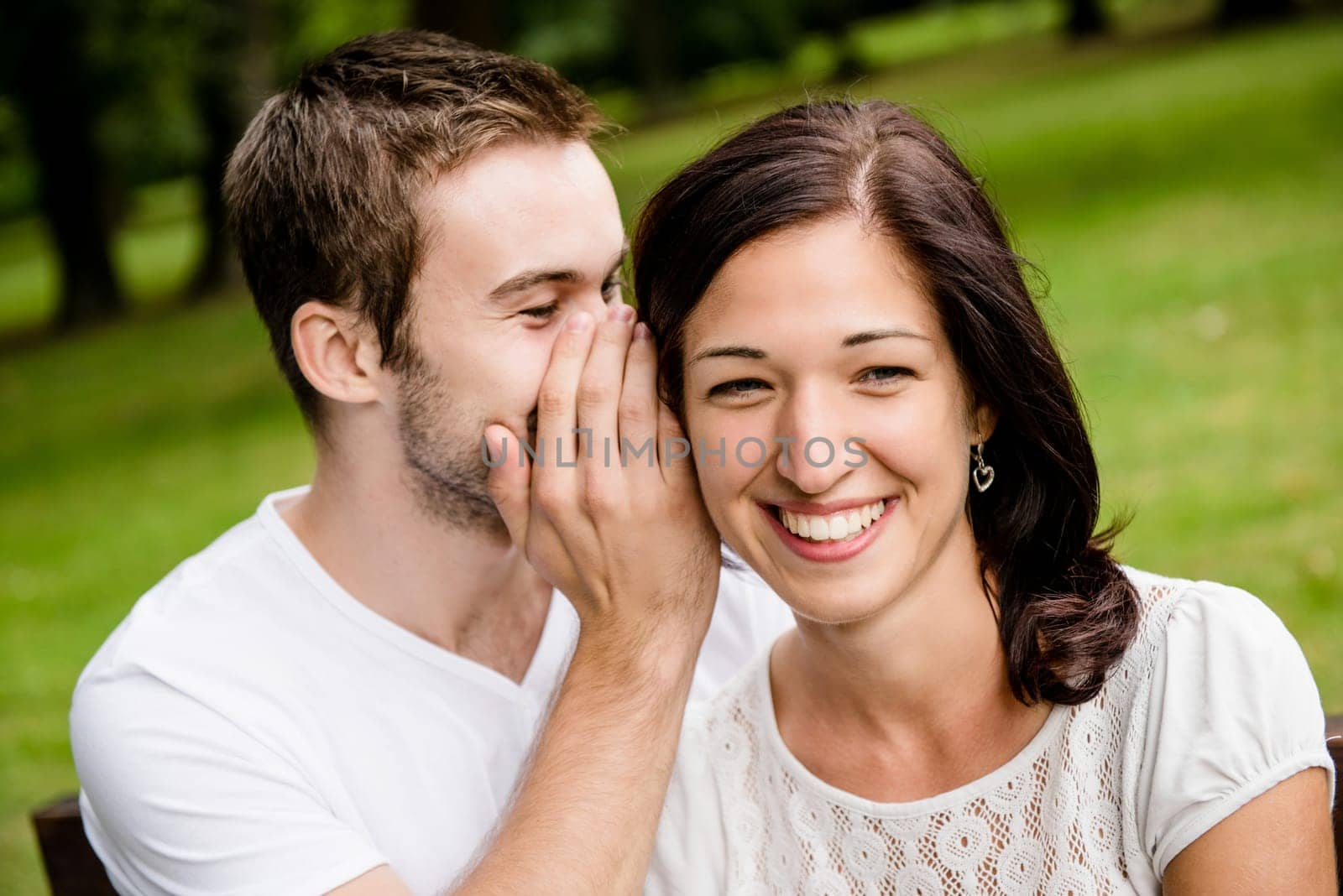 Young man whispering to woman (girlfriend) - outdoor lifestyle photo