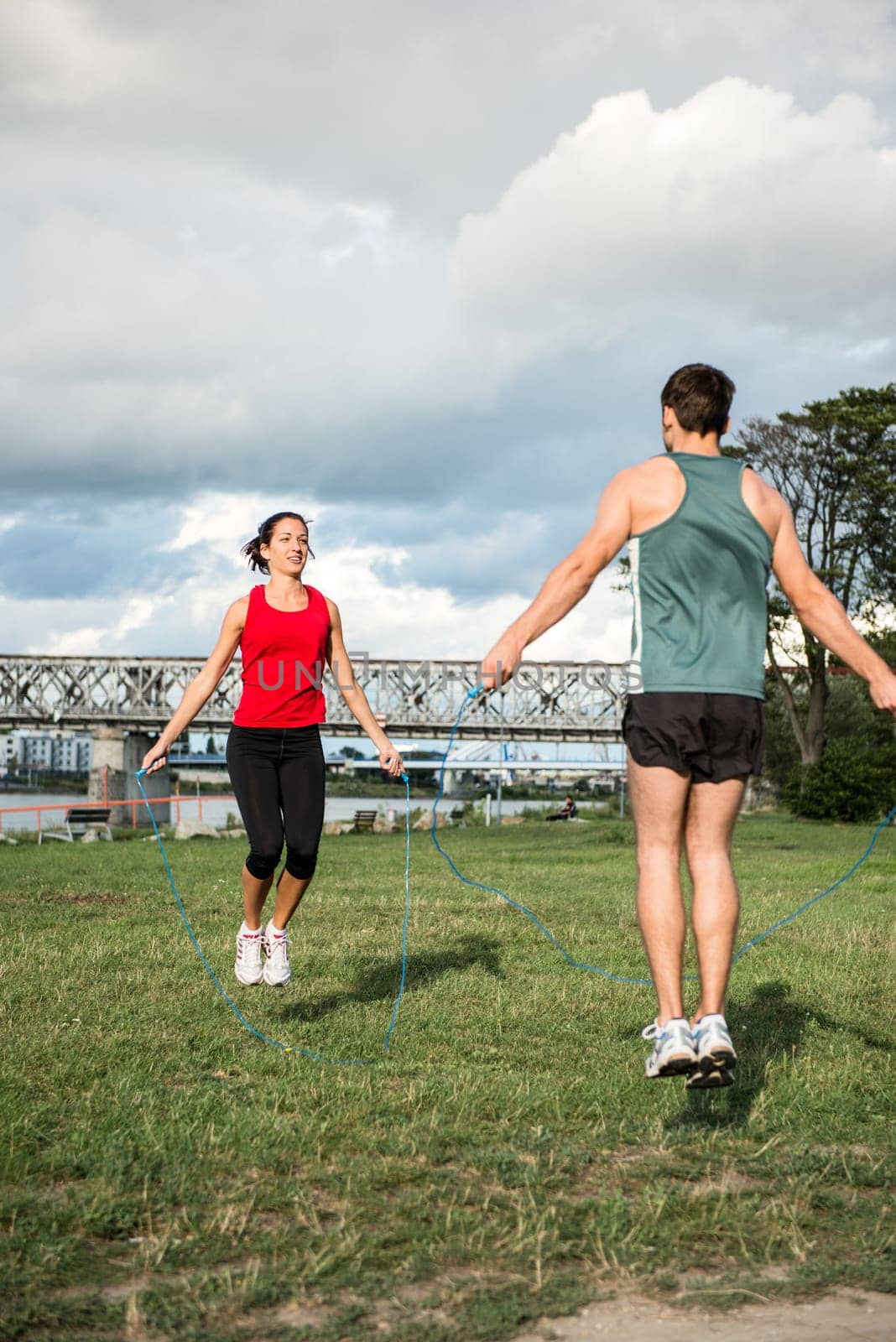 Young fitness couple exercising outdoor - jumping with skipping rope