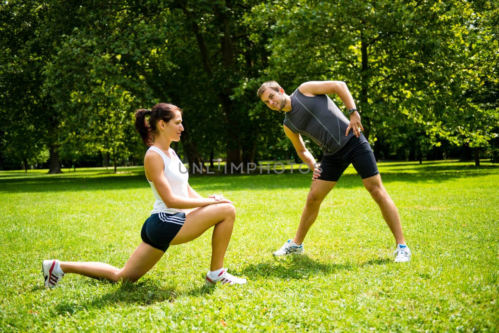 Young man and woman exercising and stretching muscles before sport activity - outdoor in nature