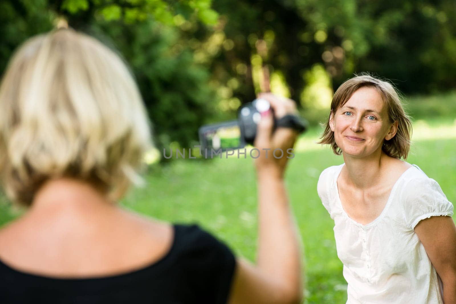 Senior mother is taking video of her adult daughter in nature with camcorder